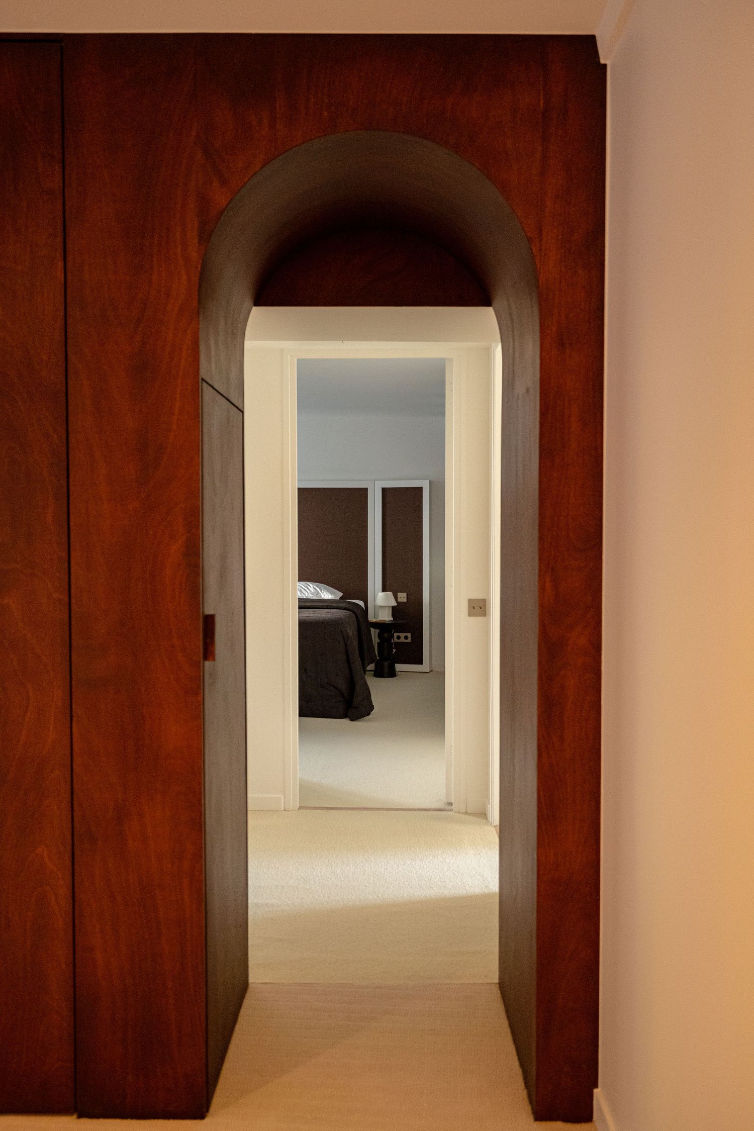 Elegant arched mahogany doorway leading to a softly lit bedroom with neutral tones.