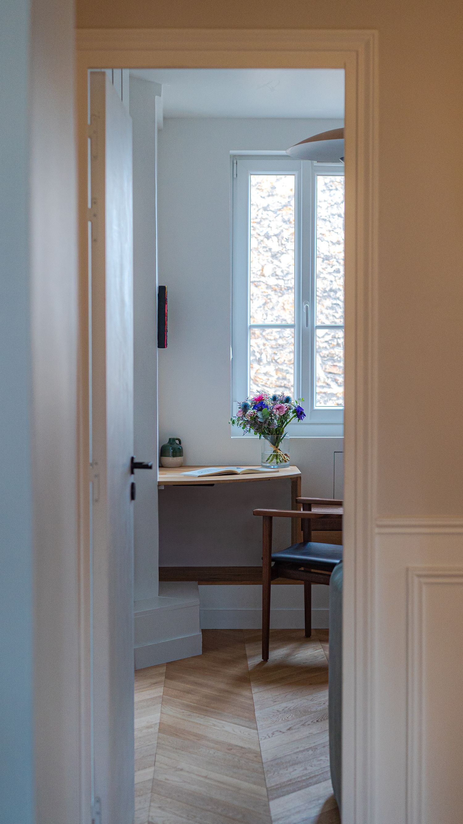Elegant Parisian apartment doorway revealing a home office with herringbone floors, wooden desk, and fresh flowers.