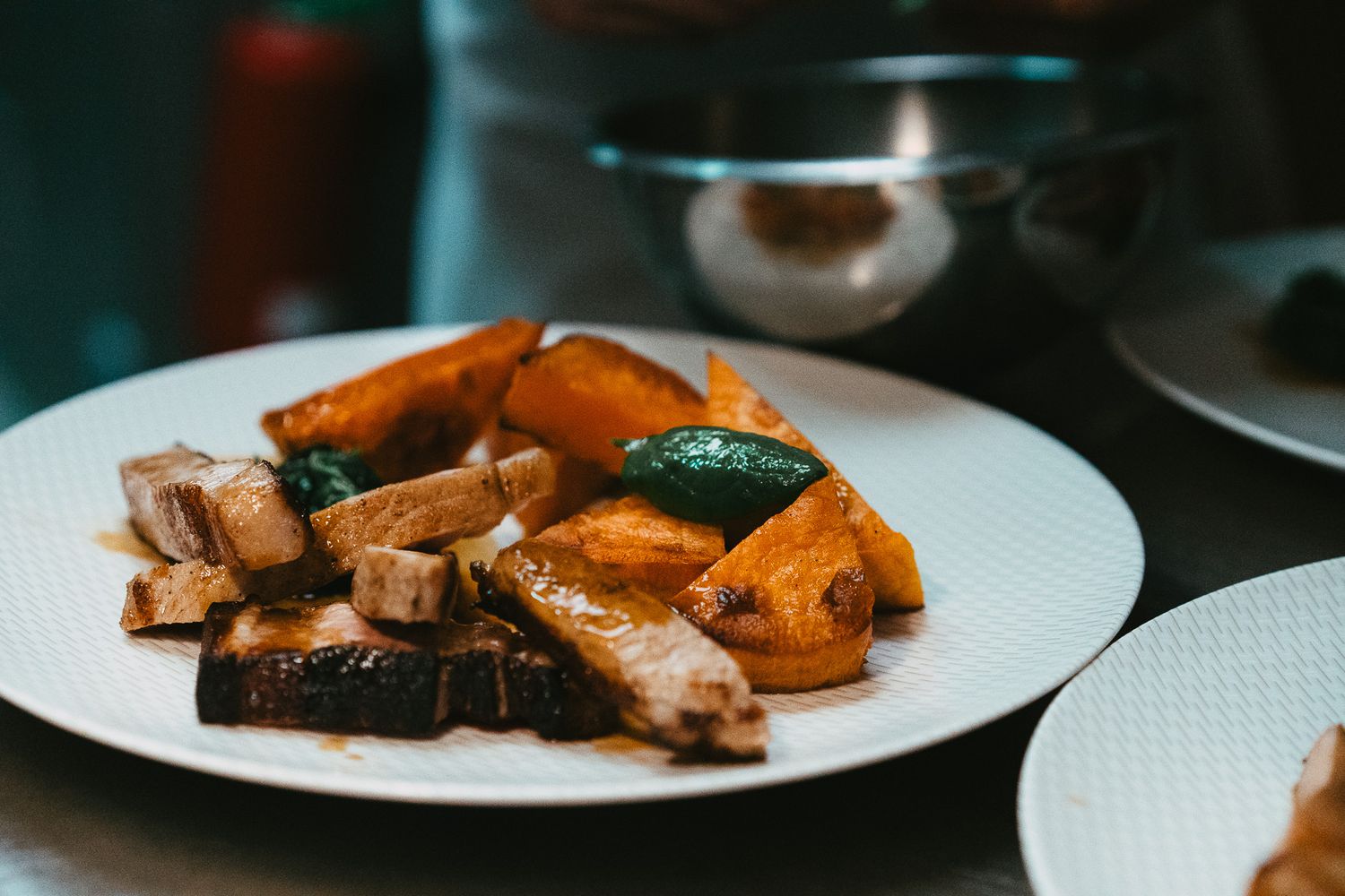 Roasted pumpkin and pork belly with sage leaves on a white plate at a fine dining restaurant.