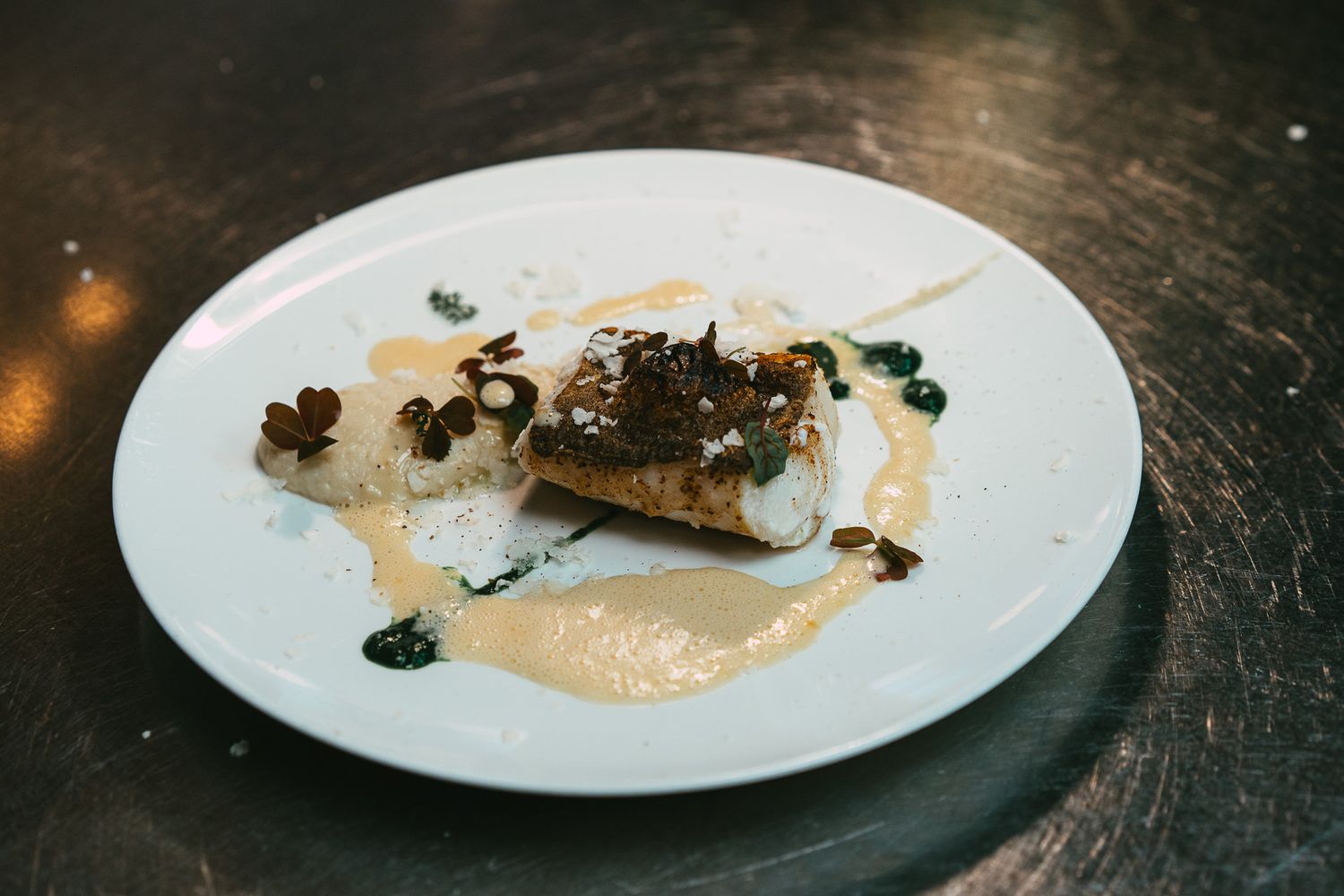 Gourmet pan-seared fish fillet with mushrooms, seeds, and creamy sauce plated on a white dish.