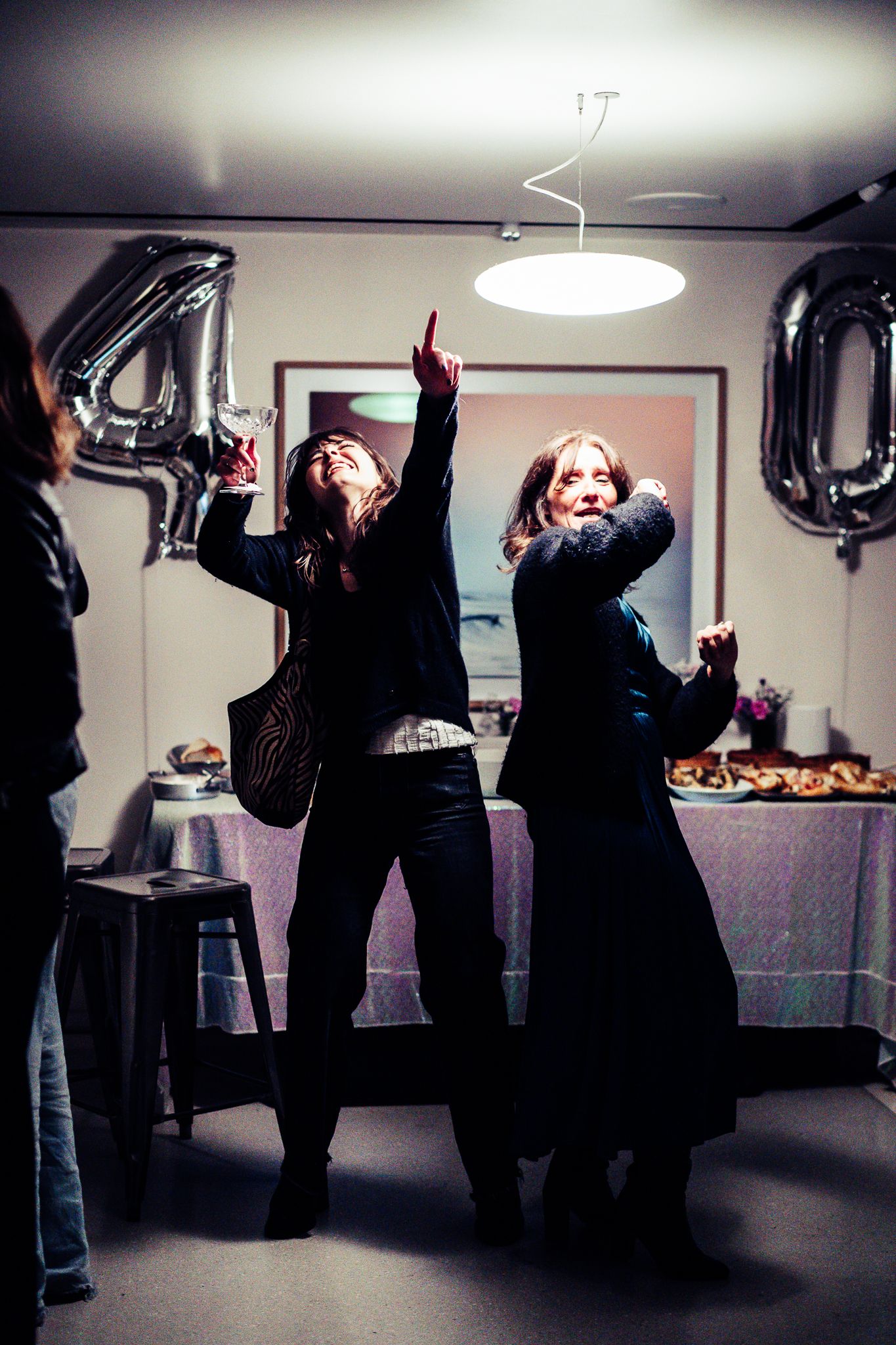 Two women dancing joyfully at a 40th birthday party with silver balloon decorations.