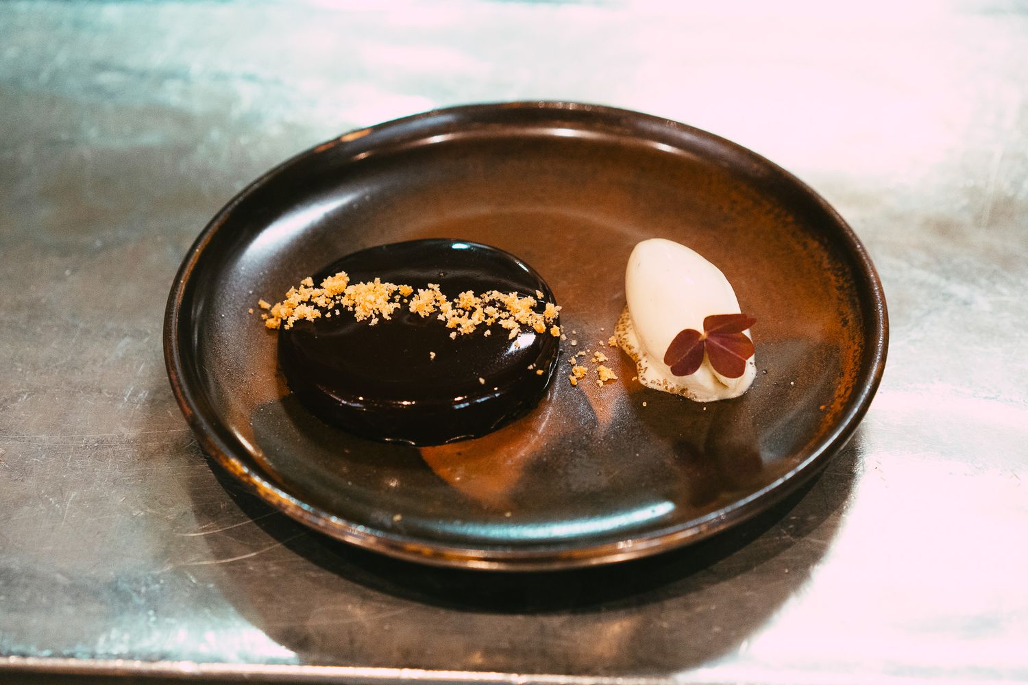 Elegant chocolate dessert with ganache, ice cream, and crunchy toppings on a dark ceramic plate.
