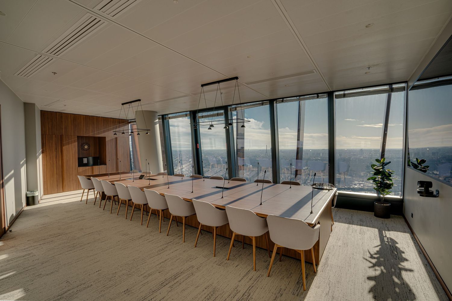 Modern high-rise conference room with long white table, upholstered chairs, wood paneling, and panoramic city views.