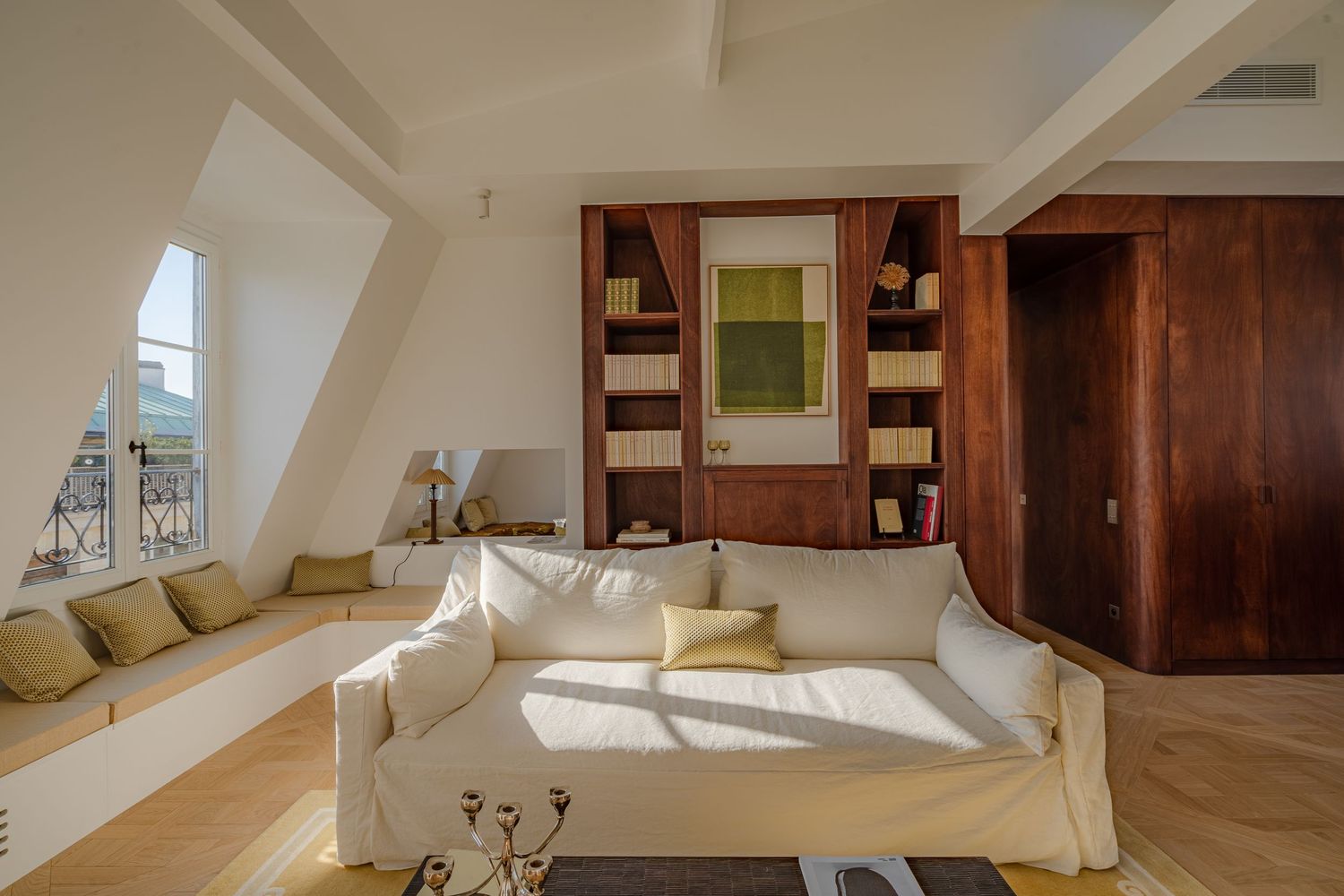 White sofa with yellow cushions in a bright attic living room with wooden built-in shelves and window seat.