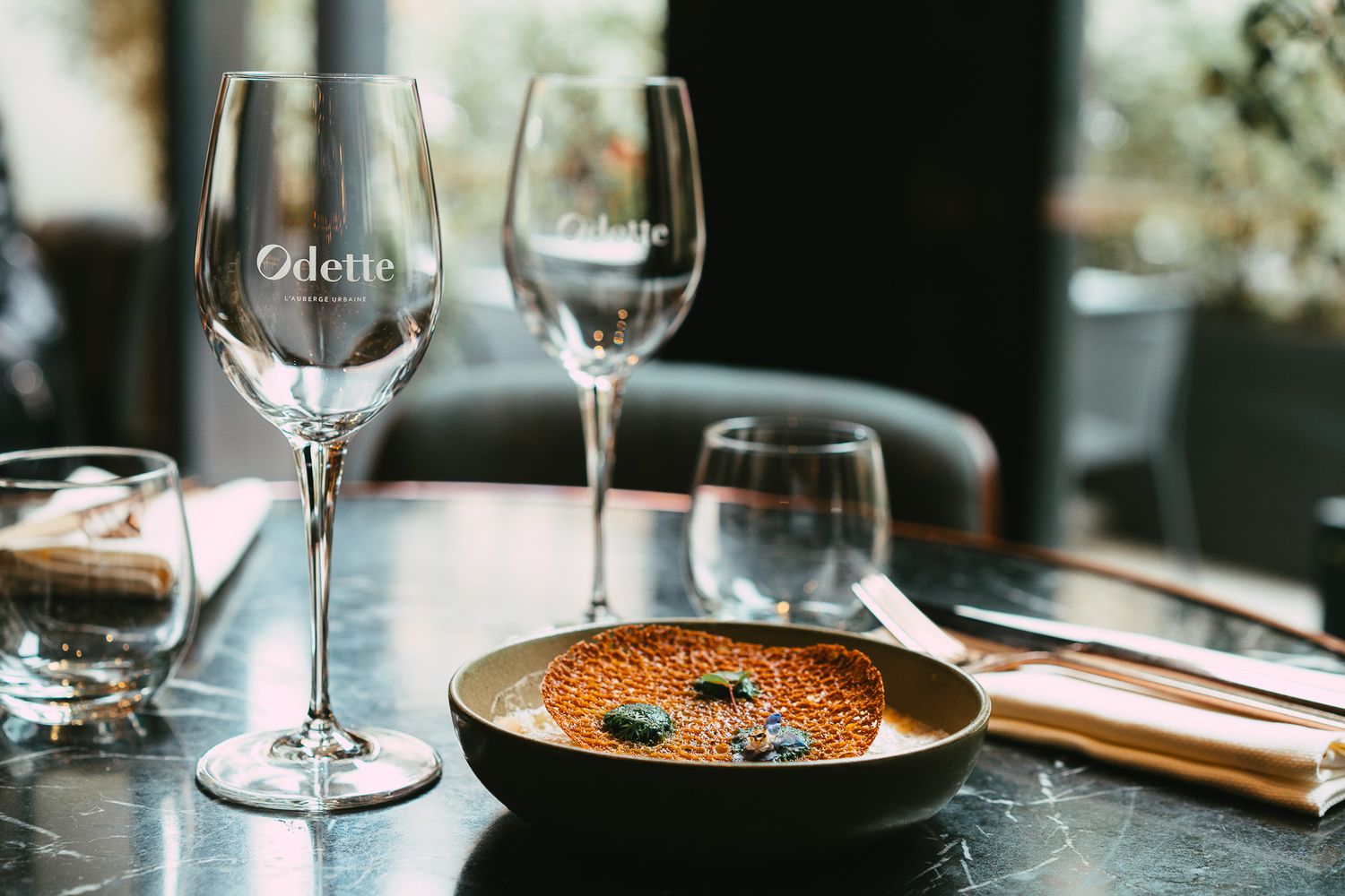 Fine dining dish in ceramic bowl with Odette wine glasses on marble table.