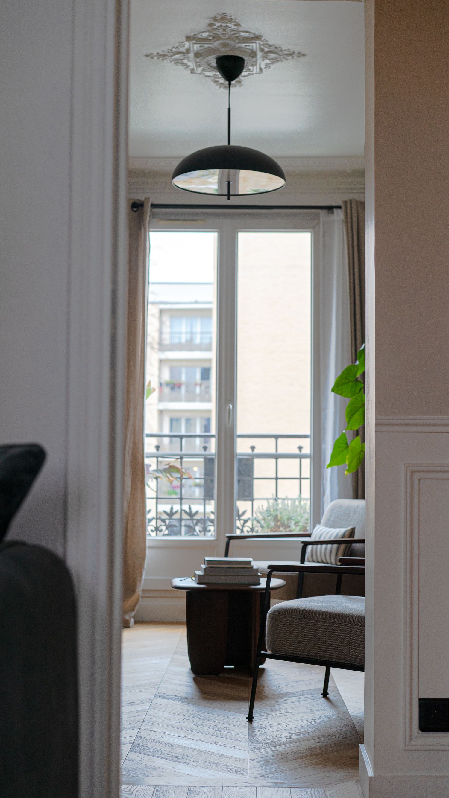 Elegant Parisian apartment hallway view with herringbone floors, ornate ceiling medallion, and balcony window.