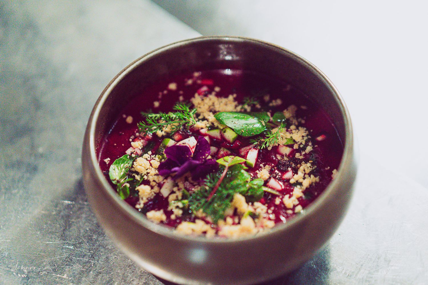 Vibrant beet soup with quinoa, fresh herbs, and edible flowers in a rustic ceramic bowl.