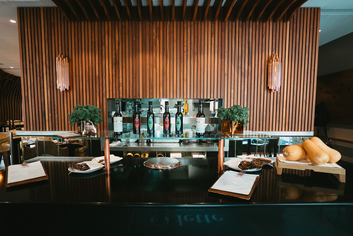 Elegant restaurant bar with wooden wall panels, bottles, and fresh bread on a dark counter.