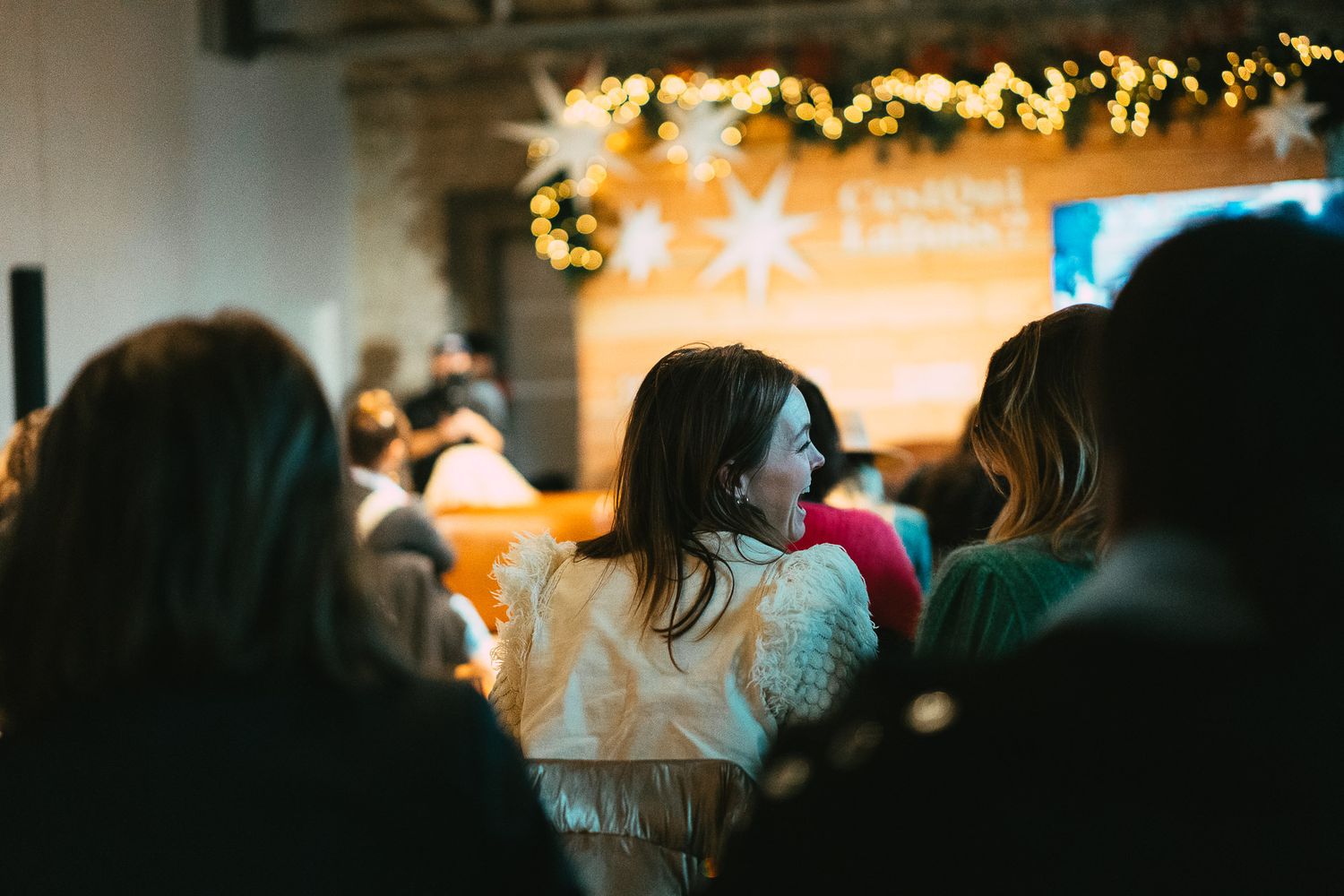Audience members at a festive indoor event with star decorations and warm string lights overhead.