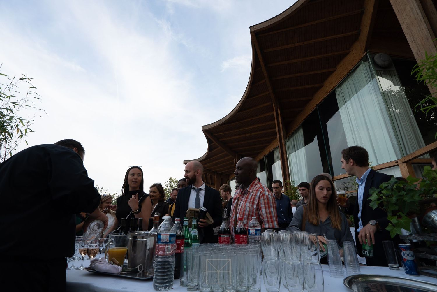Guests mingle at an outdoor evening cocktail reception with a bar setup and elegant glassware.