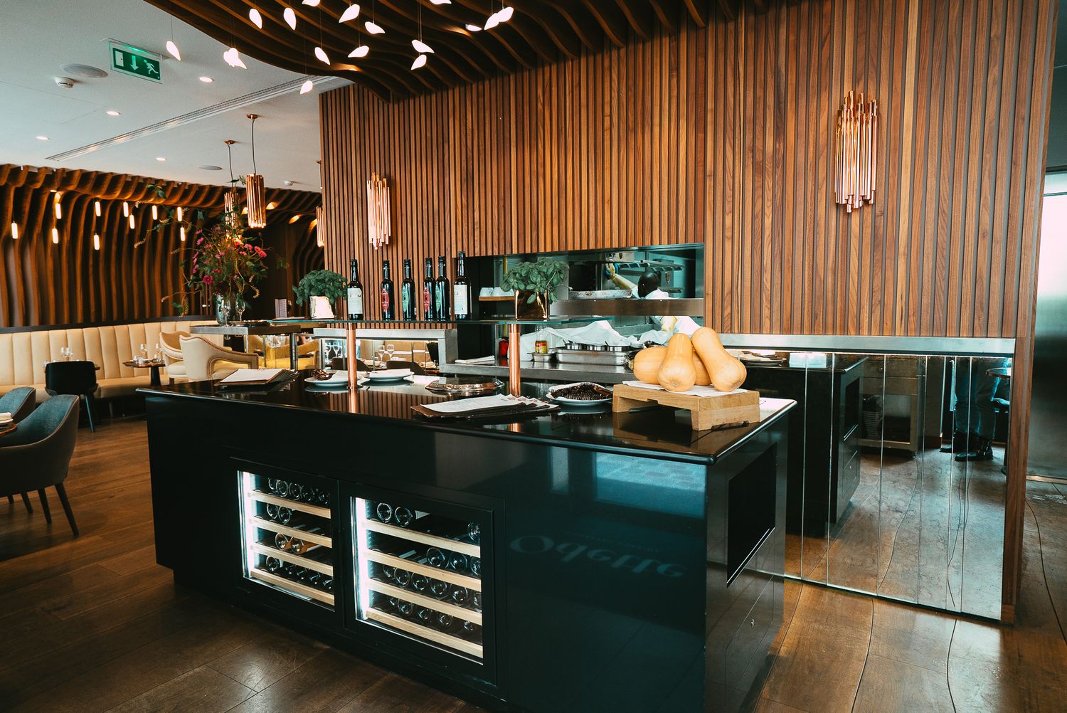 Modern restaurant interior with dark central island, built-in wine cooler, wood slat walls, and casual dining seating.
