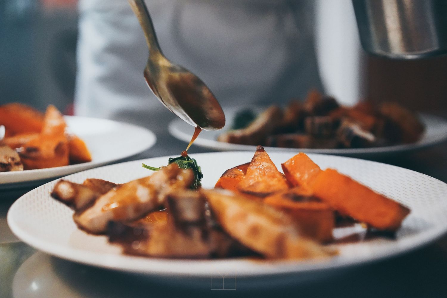 Chef plating roasted chicken and caramelized carrots with sauce in an upscale restaurant kitchen.