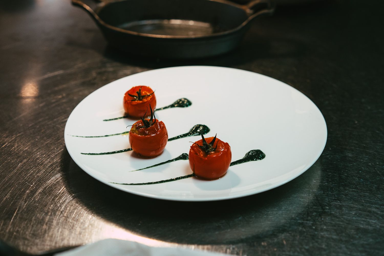 Three roasted cherry tomatoes with herb sauce drizzles arranged on a white plate in a fine dining presentation.