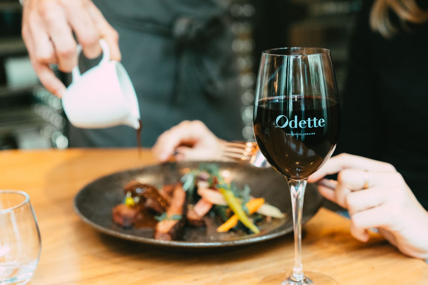 An Odette branded wine glass beside a gourmet dish being plated at an upscale restaurant.
