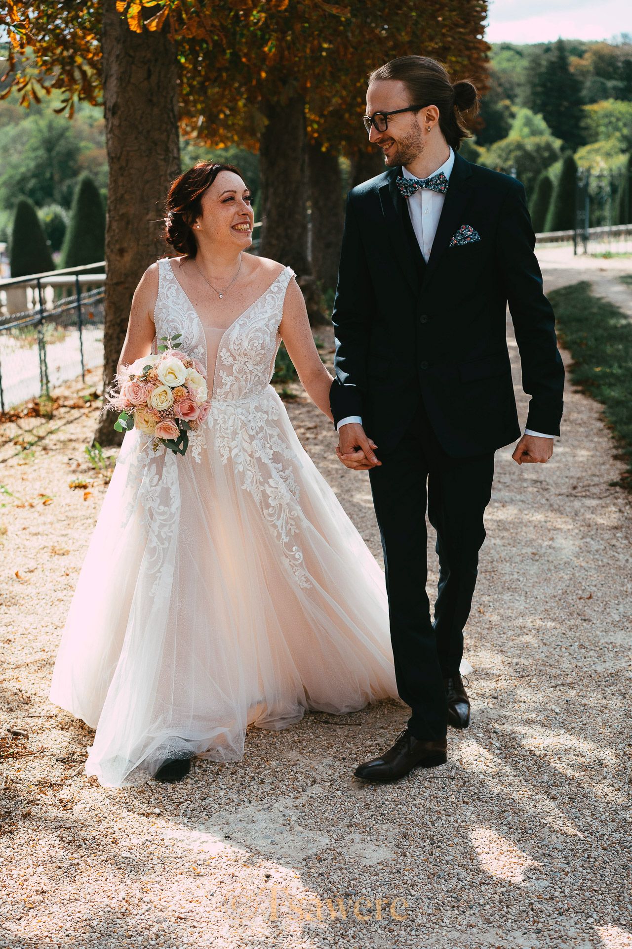 Smiling bride and groom walking together in autumn park, bride holding pink floral bouquet.