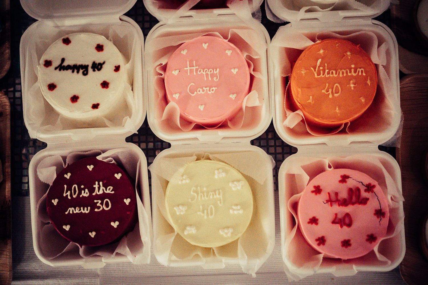 Six decorated mini cakes with 40th birthday messages in colorful frosting in individual boxes.