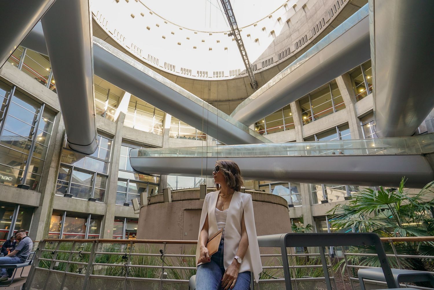 Woman in beige blazer walking through modern architectural atrium with steel beams.