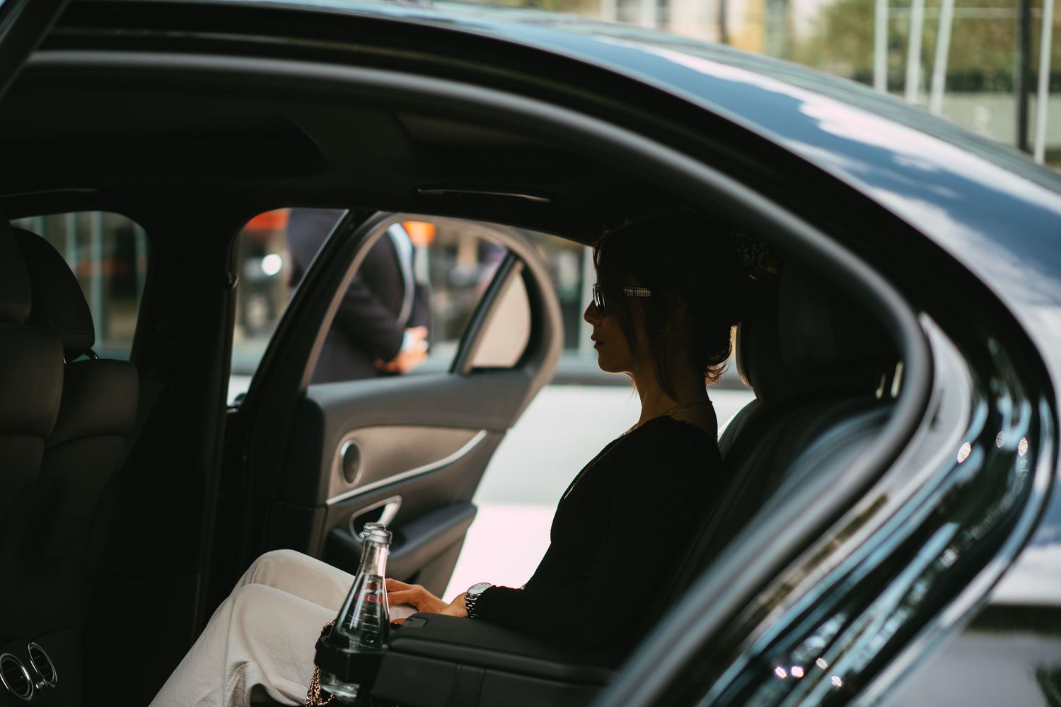 Woman sitting in the back seat of a luxury black car in an urban setting.