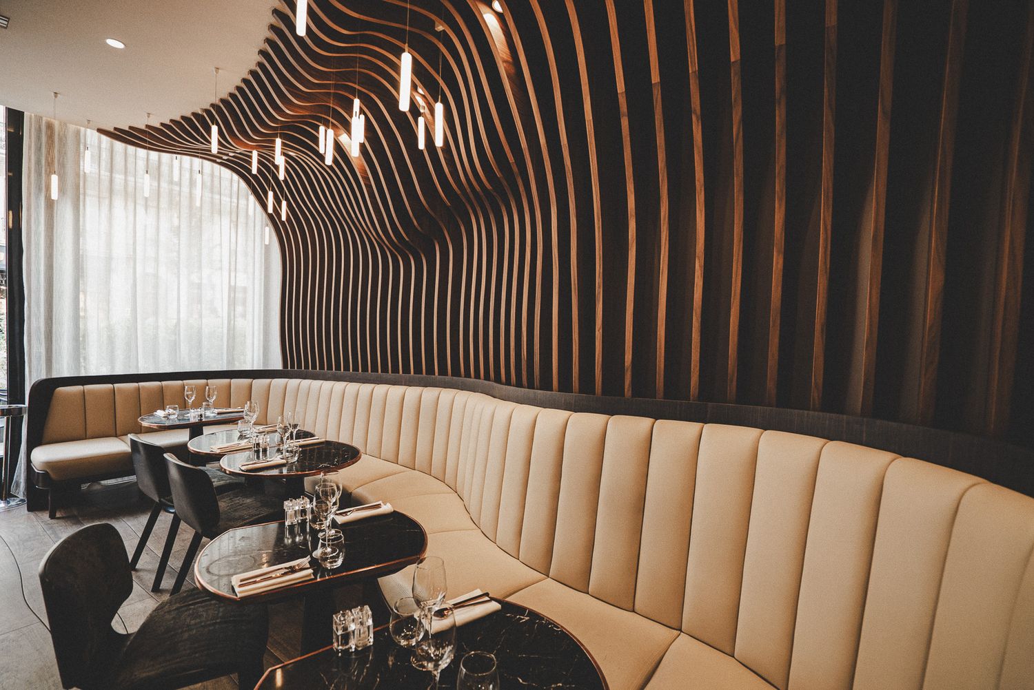 Luxurious restaurant booth seating with cream upholstery and curved wooden wave-pattern walls.