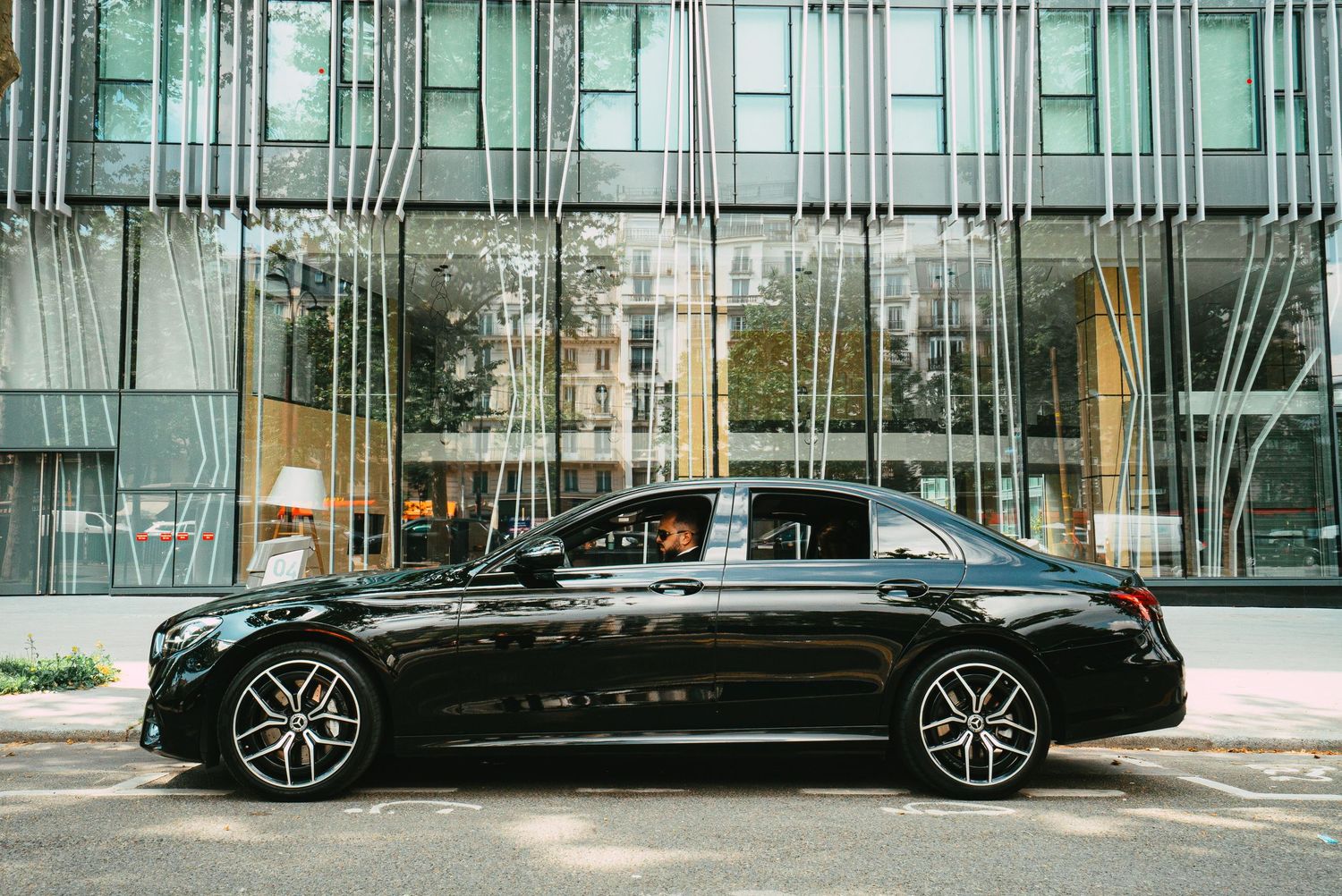Black Mercedes-Benz E-Class luxury sedan parked outside modern glass building.