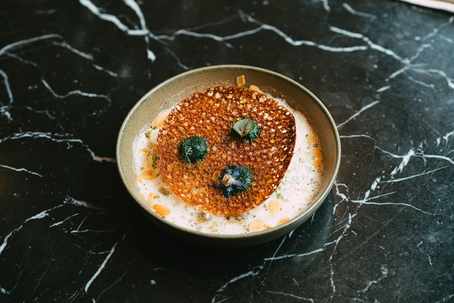 Gourmet soup bowl with crispy tuile, caviar, and herb garnish on marble surface.