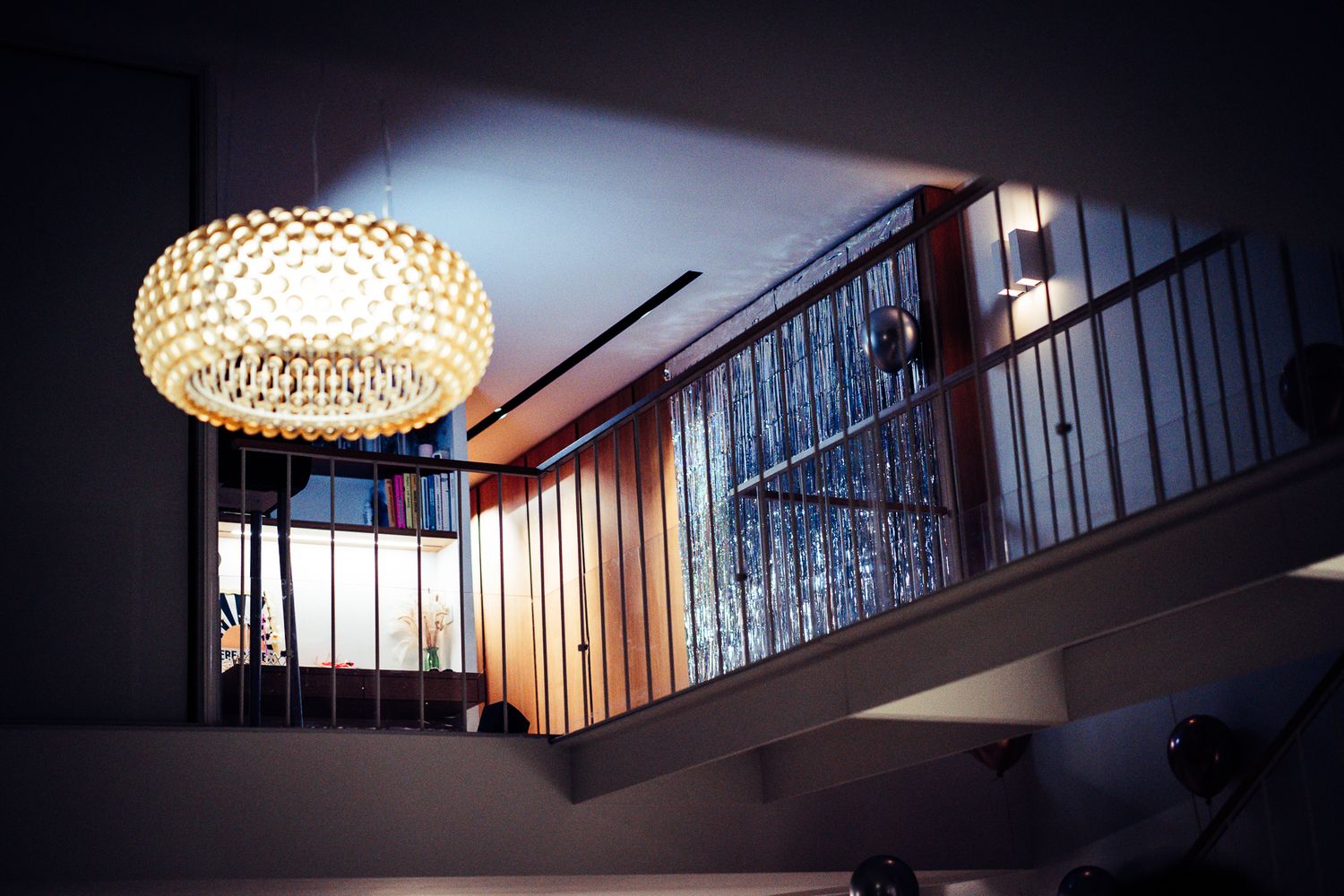 Modern interior staircase with elegant crystal pendant chandelier illuminating a mezzanine level with wooden railings.