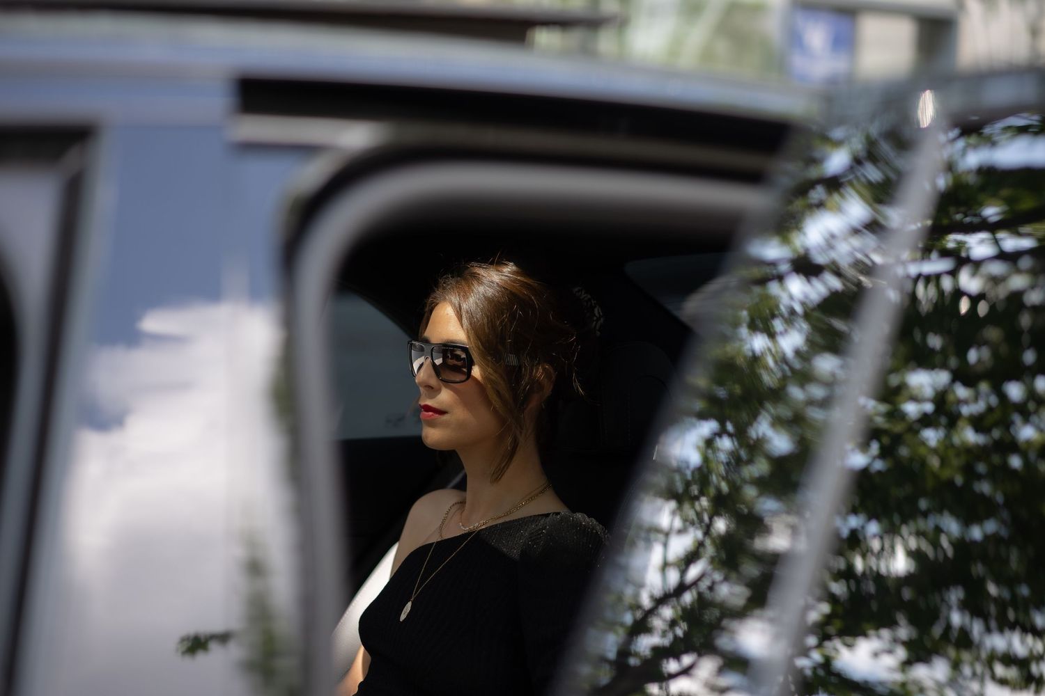 Young woman in sunglasses stepping out of a dark SUV vehicle.