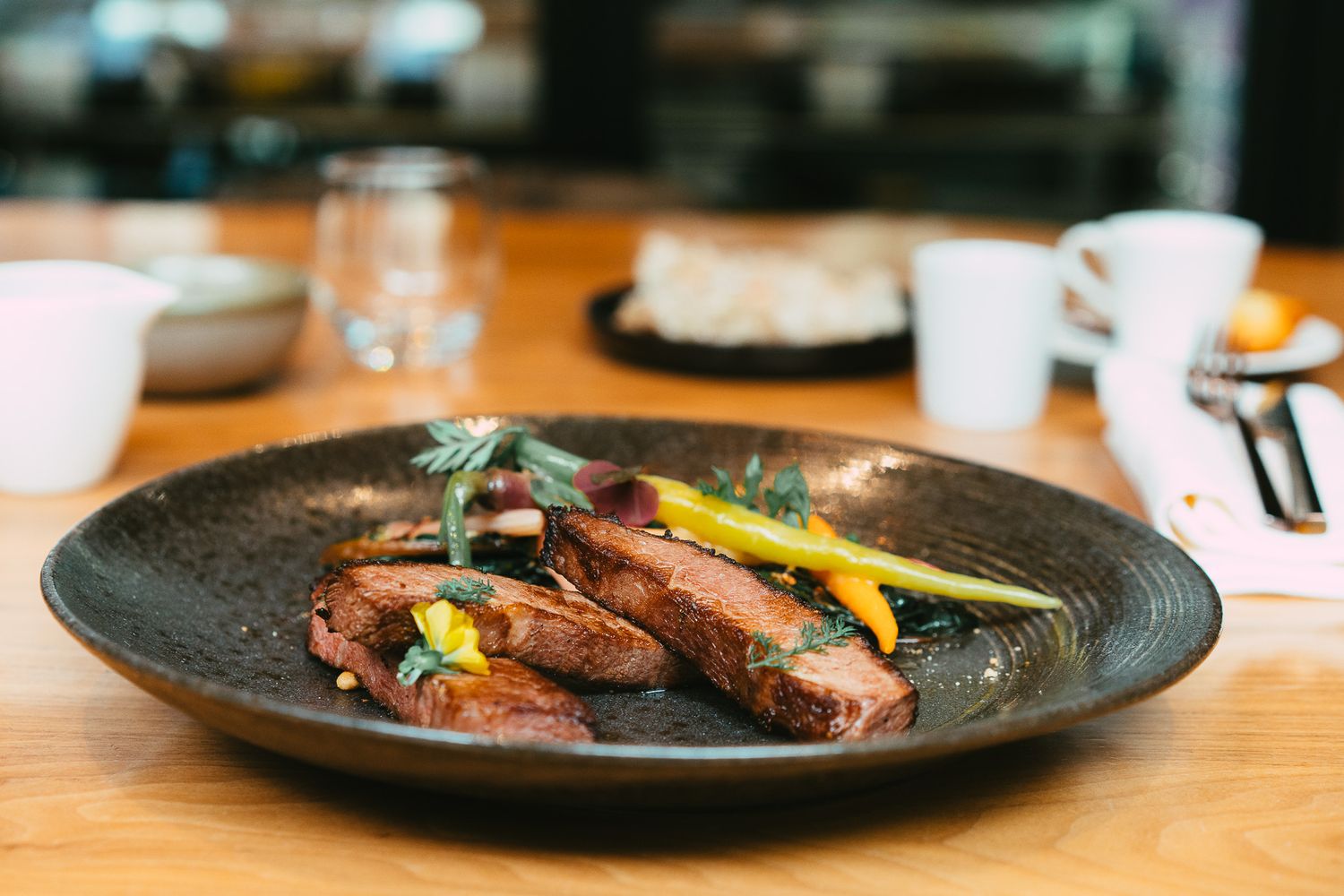 Sliced duck breast with roasted vegetables and fresh herbs on dark ceramic plate.