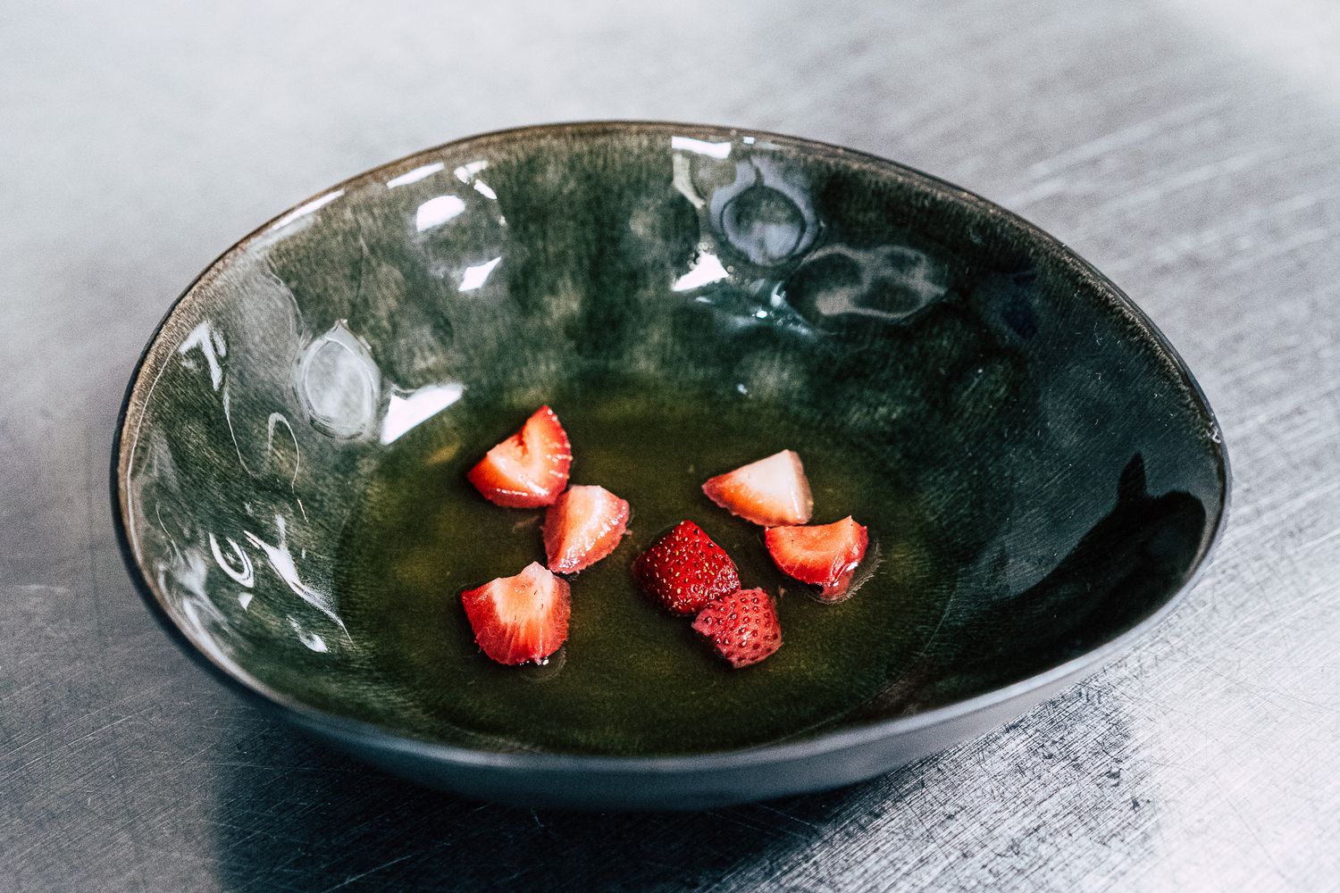 Fresh sliced strawberries arranged in a dark green ceramic bowl on a gray surface.