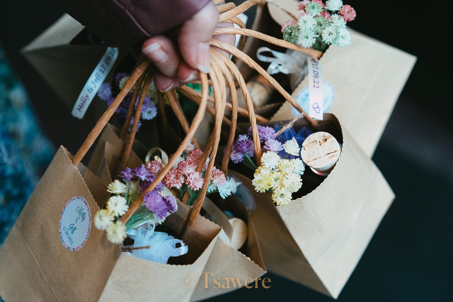 Hand holding a kraft bag filled with colorful dried flower bouquets and floral arrangements.