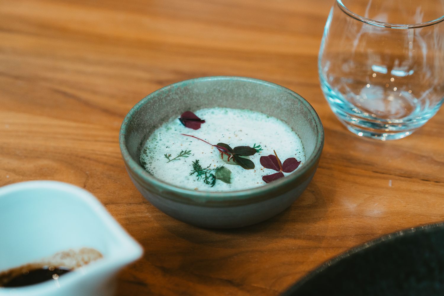 Creamy white soup garnished with fresh herbs and edible flowers in ceramic bowl.