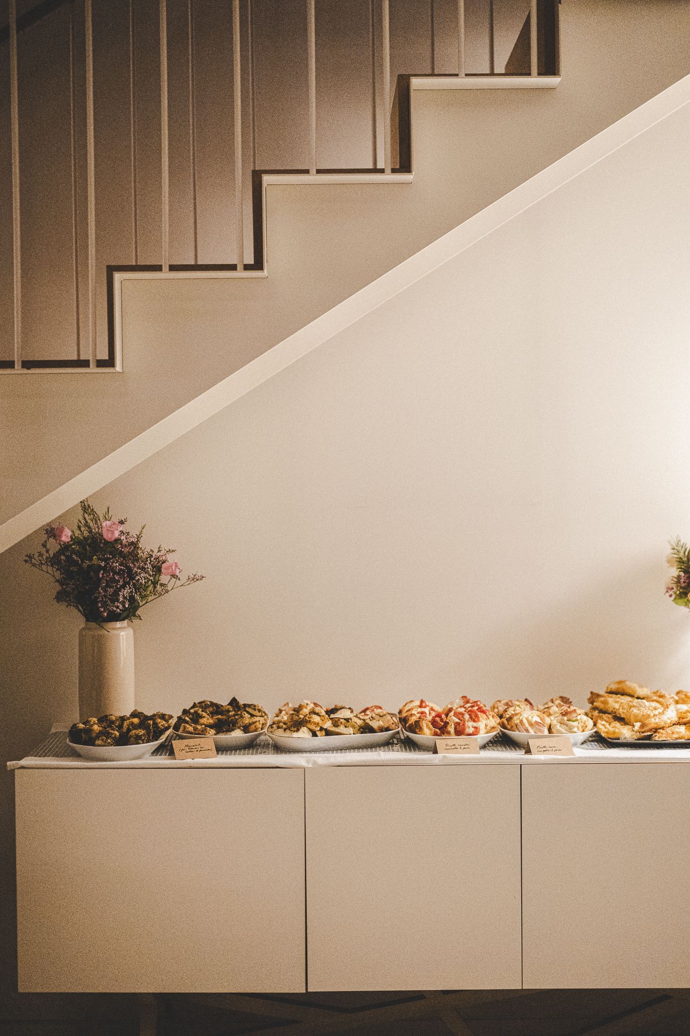 Assorted finger foods displayed on a white sideboard beneath a staircase.