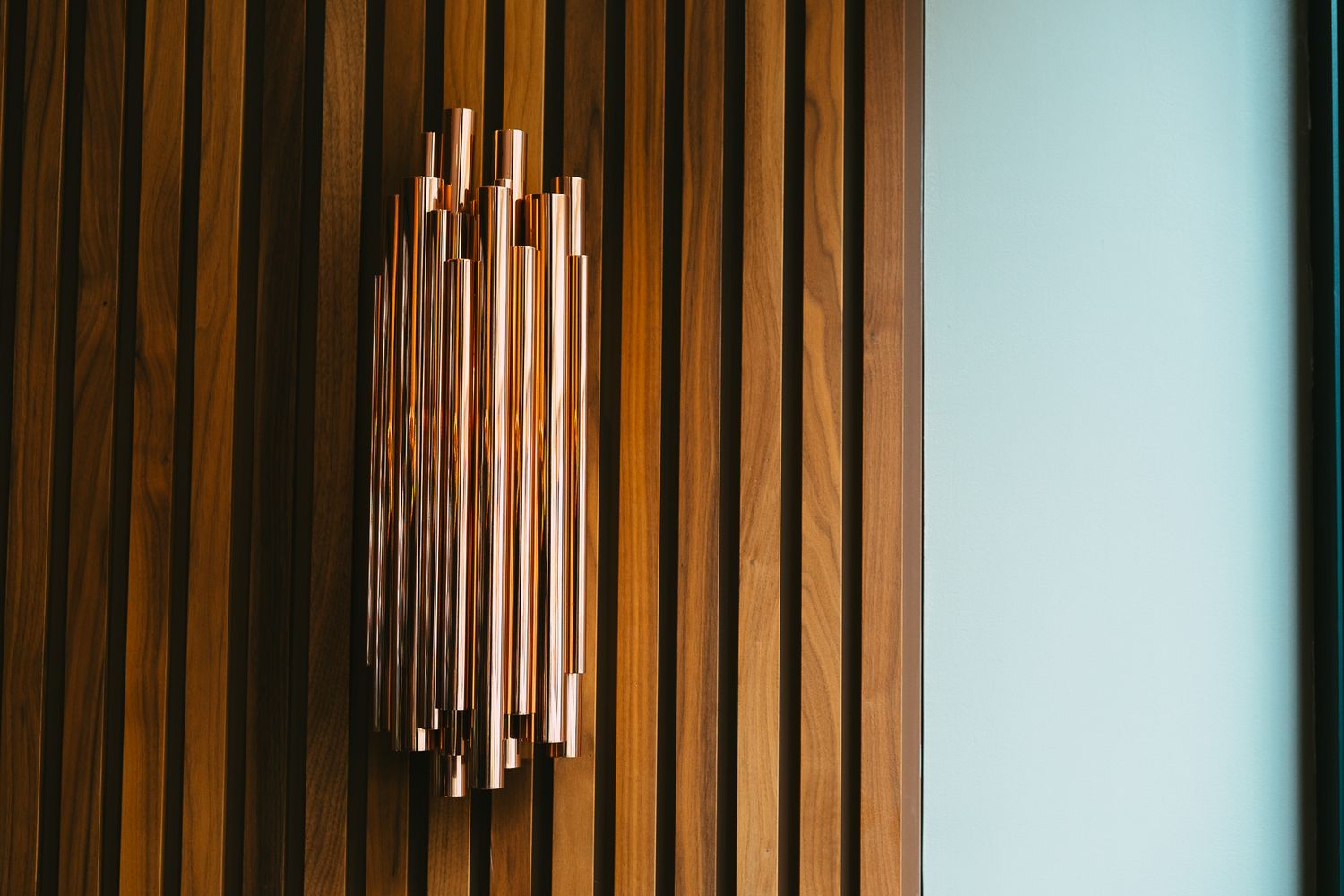A decorative copper pipe wall sconce mounted on wooden slat paneling in a modern restaurant.