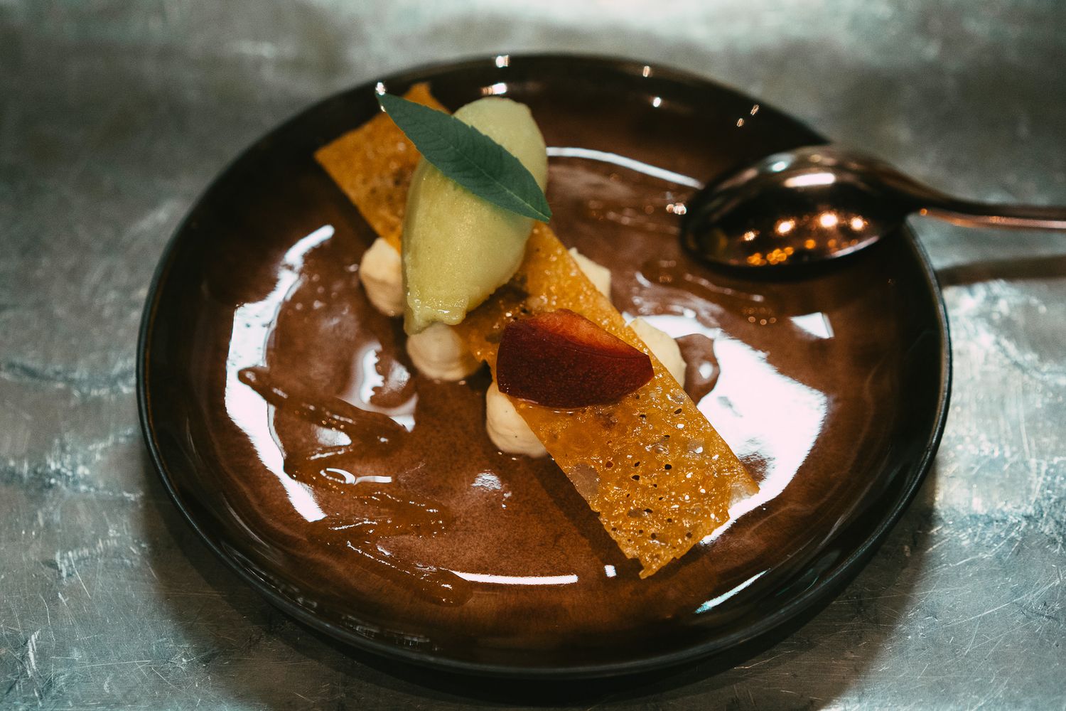 Decadent chocolate dessert with ice cream, caramel, and crispy wafer on dark plate.
