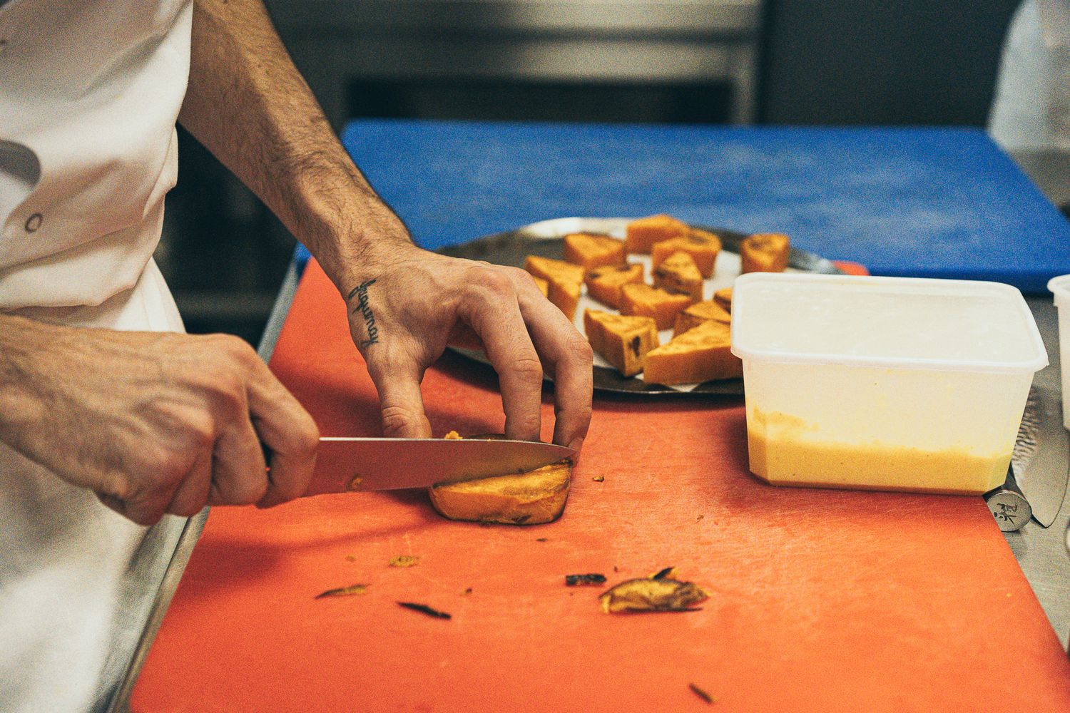 A chef slices grilled bread on a red cutting board next to a container of butter in a professional kitchen.