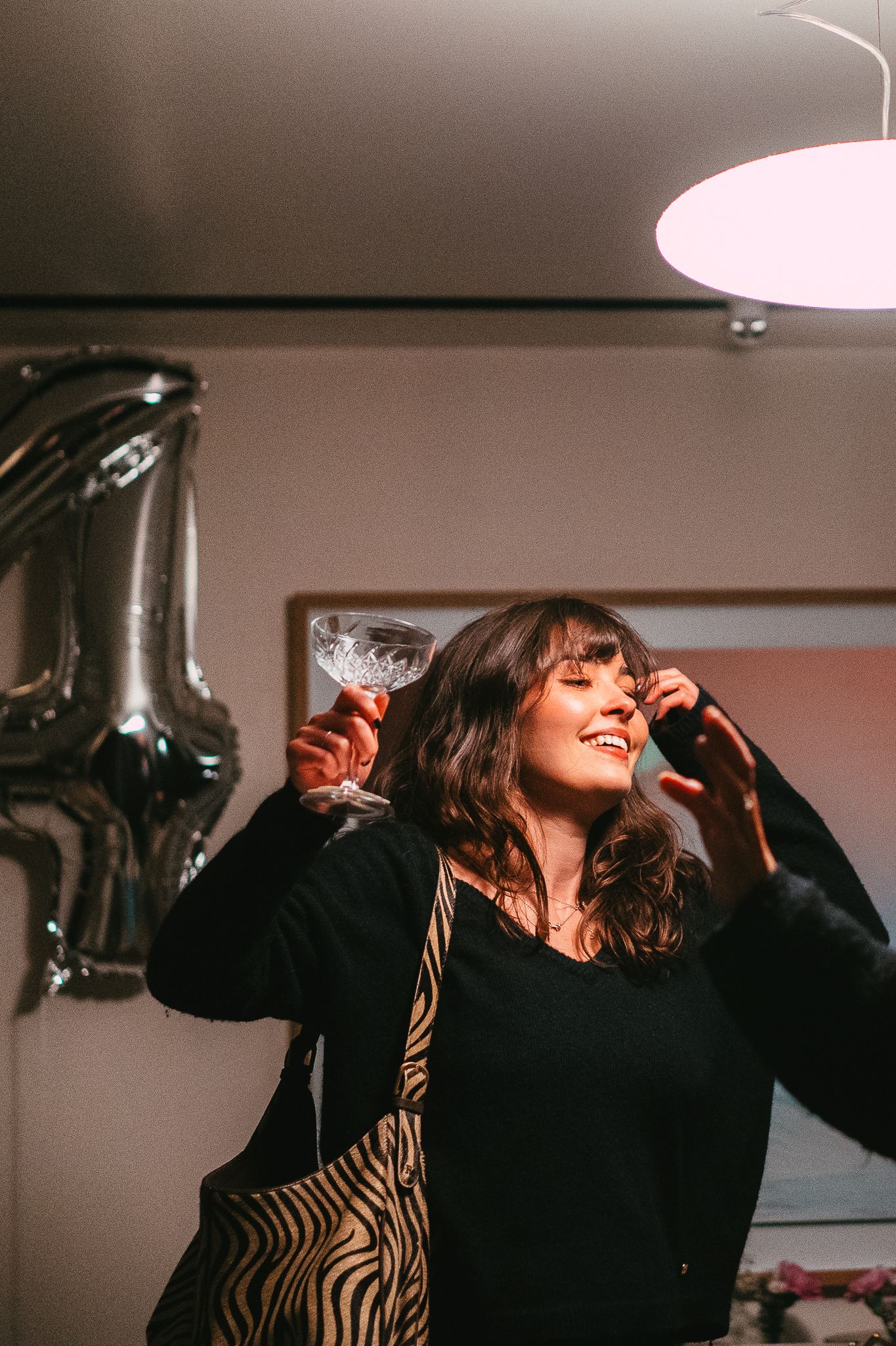 Happy woman holding a cocktail glass and dancing near a silver balloon at a party.