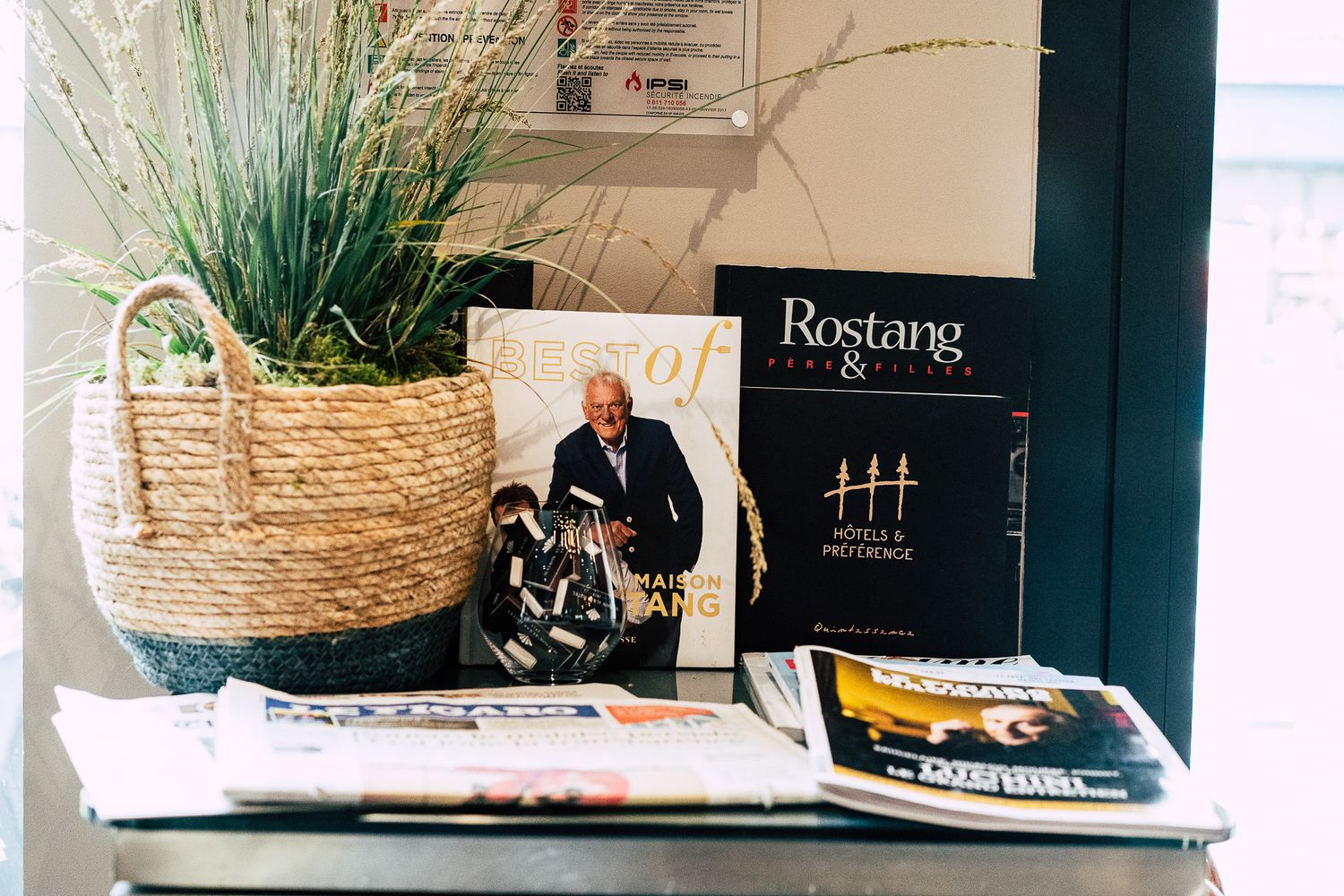 A wicker basket with grass plant beside Rostang cookbooks and magazines on a shelf.