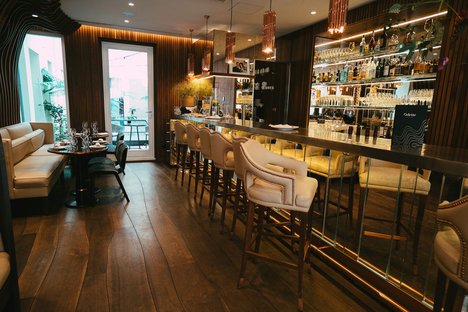 Sophisticated bar interior featuring cream bar stools, warm wood walls, pendant lighting, and an extensive spirits collection.