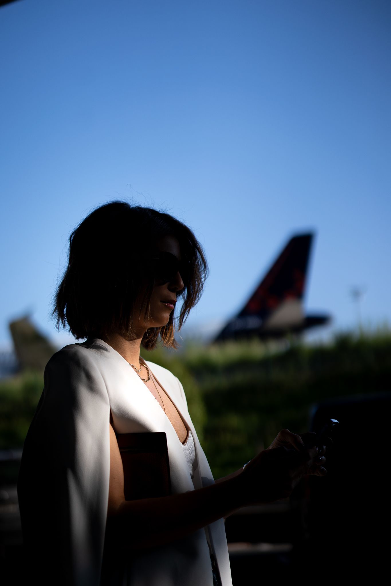 Silhouette of woman using phone with airplane tail in background.