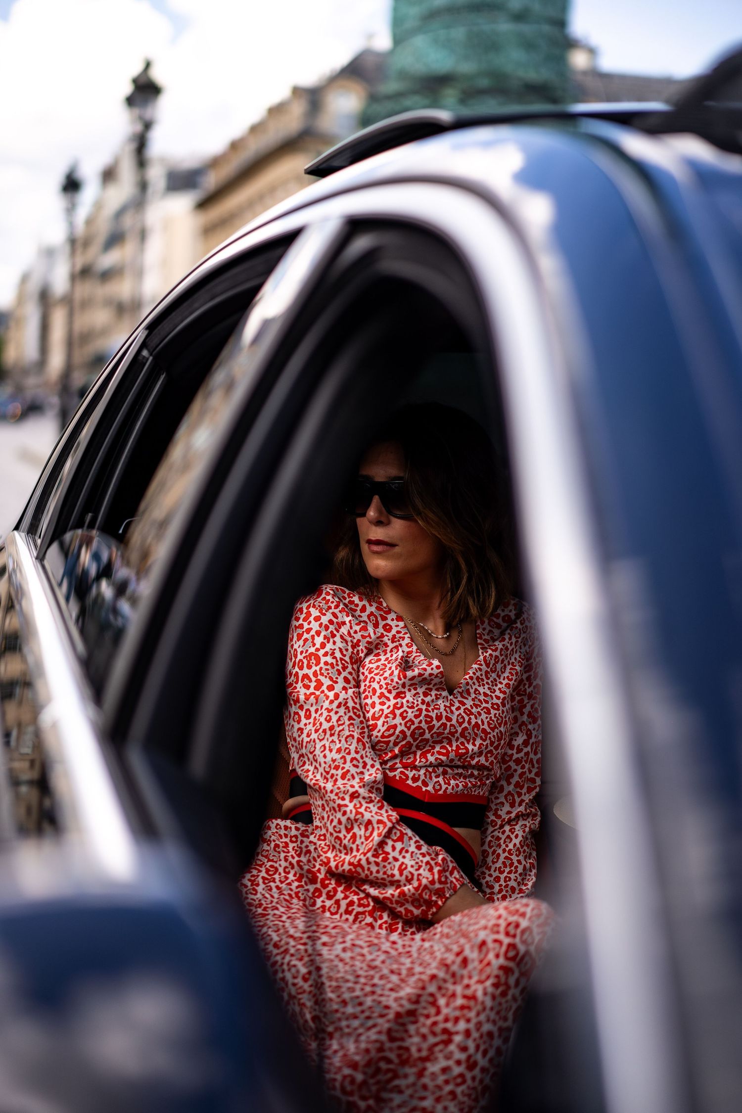Elegant woman in red leopard print dress sitting in car backseat on Paris street.