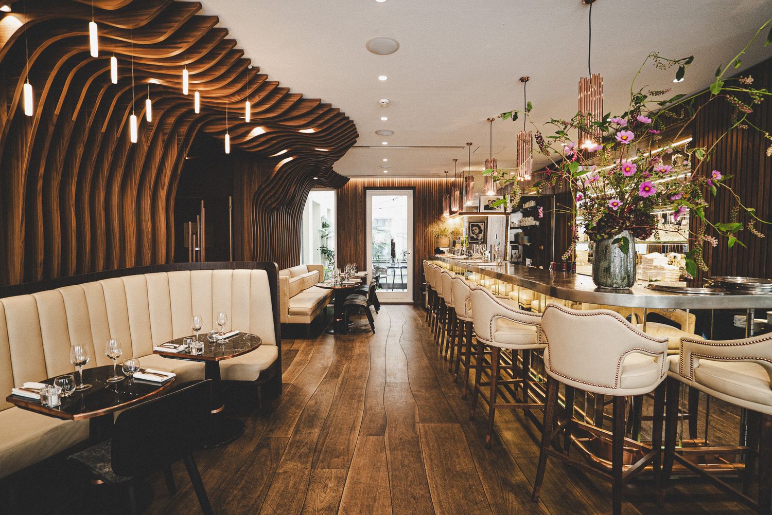 Elegant restaurant interior with curved wood paneling, cream booths, and a stylish bar area.