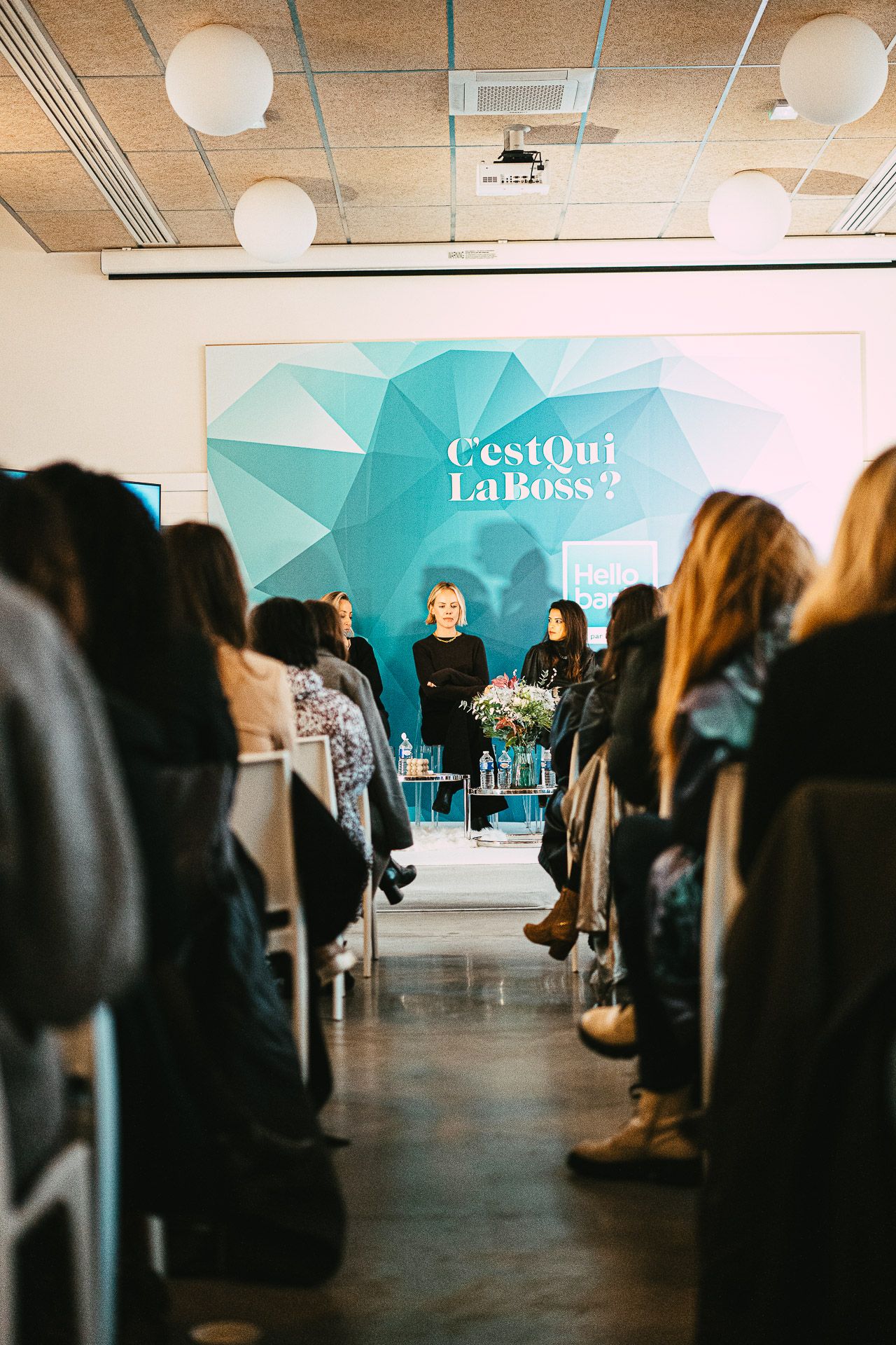 Audience seated at a C'est Qui La Boss panel discussion with teal geometric backdrop.