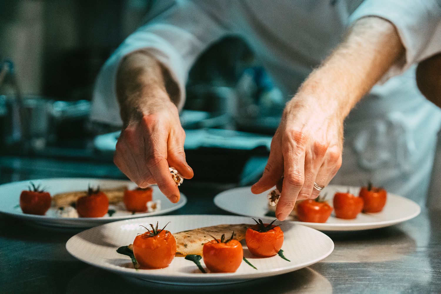 Chef garnishing cherry tomato dishes on white plates in a professional restaurant kitchen.