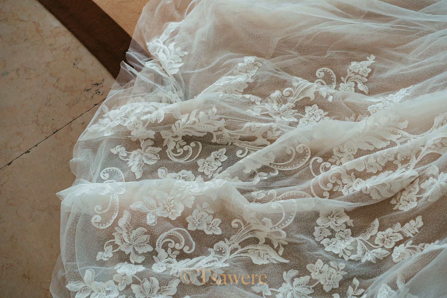 Close-up of elegant white lace wedding dress fabric with intricate floral embroidery details.