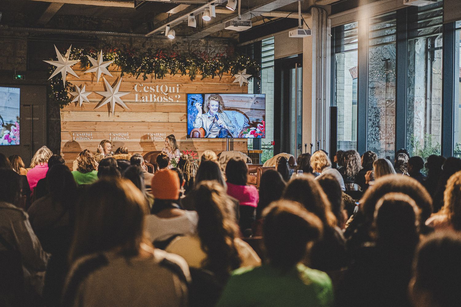 Large crowd attending a C'est Qui La Boss conference with star decorations and large screen.