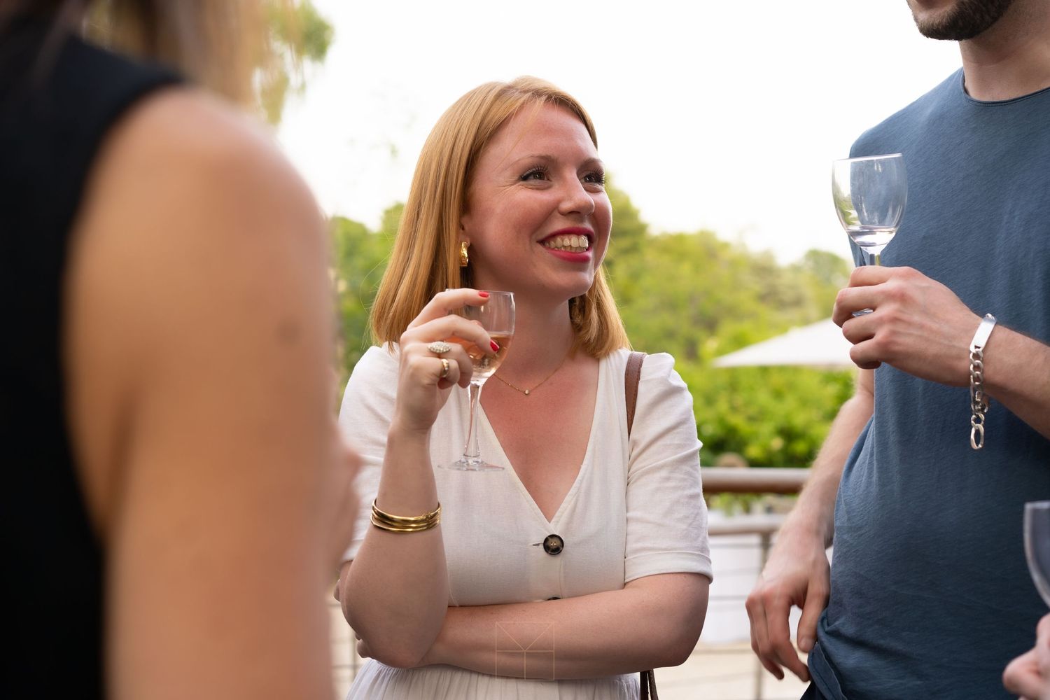 Smiling redhead woman holding wine glass socializing at an outdoor garden party event.