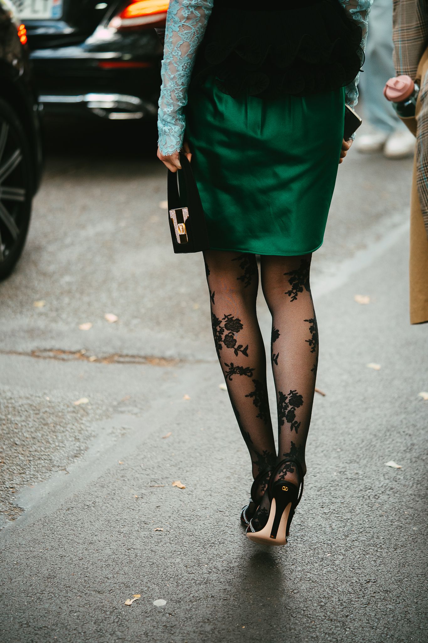 Close-up of floral black sheer tights with green mini skirt and heels on city street.