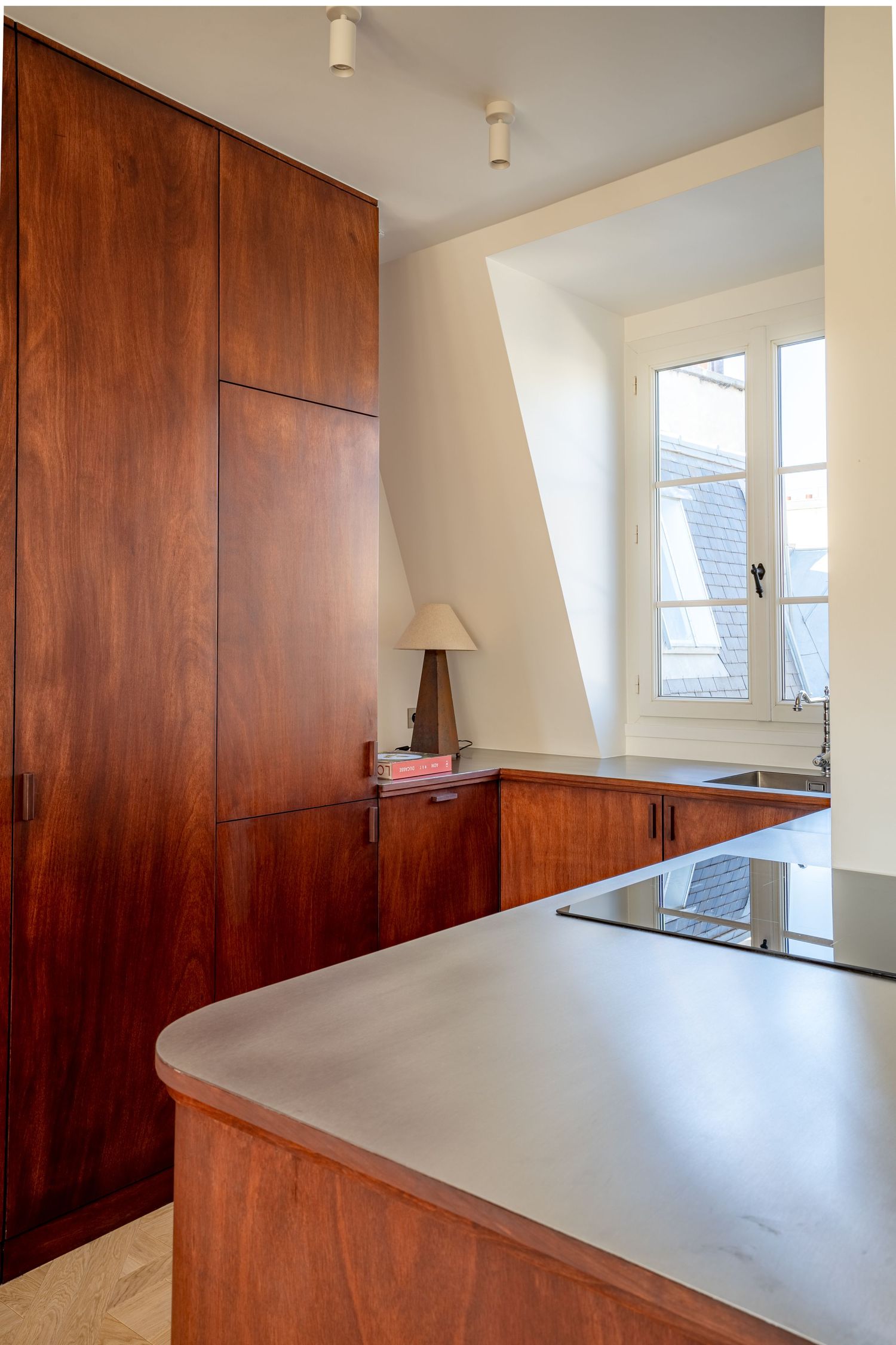 Modern kitchen with rich mahogany cabinetry, concrete countertop, and angled attic window.