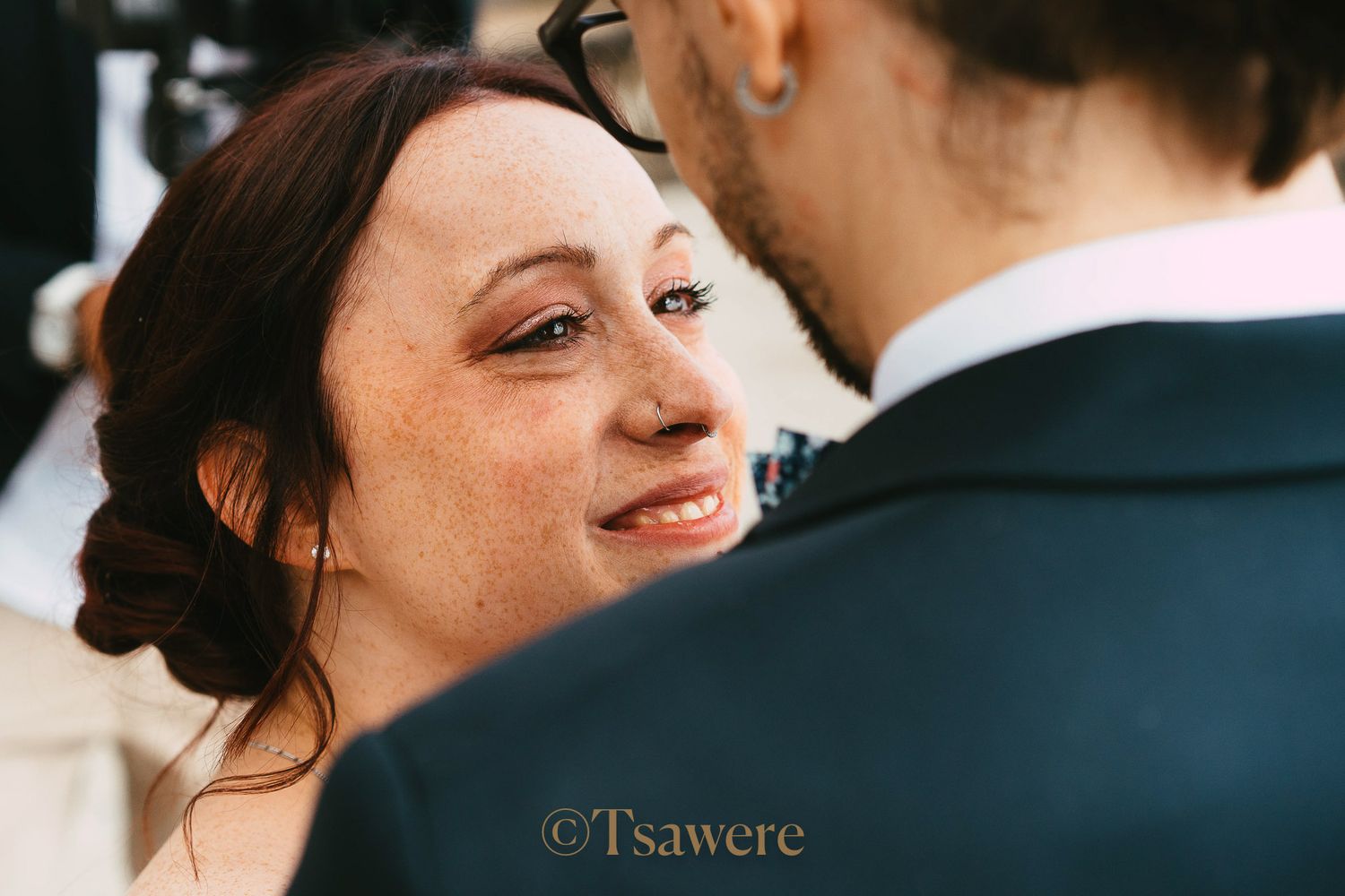 Bride with freckles and updo hairstyle gazing lovingly at groom during wedding ceremony.