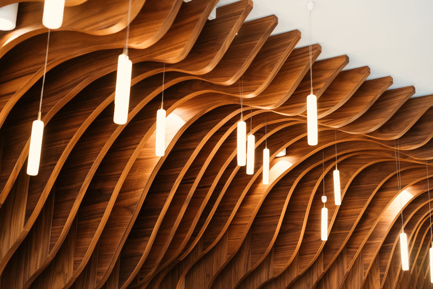 A stunning wavy wooden ceiling with pendant lights in a modern upscale restaurant interior.